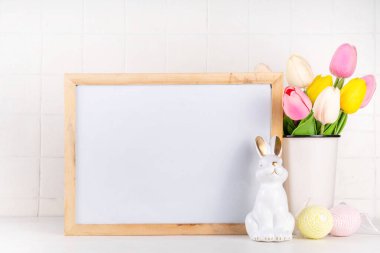 Bahar Paskalya bayramı masası boyalı Paskalya yumurtaları, bahar çiçekleri buketi, dekoratif tavşanlar, beyaz mutfak arka planında