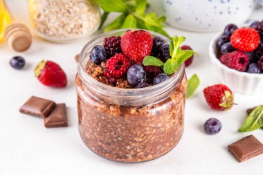 Çikolatalı Yulaf ezmesi, çikolata soslu, fındıklı ve taze dutlu, beyaz mutfak masasında yuvarlanmış yulaf, ahududu, yaban mersini, çilekli