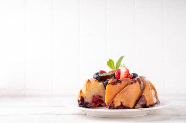 Taze meyve ve böğürtlenli yaz pastası. Geleneksel yuvarlak sünger keki, çilekli mevsimlik tatlı, ahududu, yabanmersini, bal ve şeker serpintileri, beyaz ahşap masa fotokopisi alanı