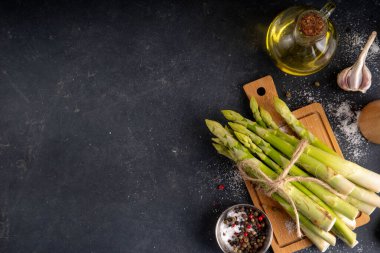 Çiğ organik kuşkonmaz mutfak masasının arka planında bir sürü ev yapımı yeşil kuşkonmaz pişirmeye ve kesme tahtasının üzerinde hazır. Yaz hasadı, yaz yemeği malzemeleri.