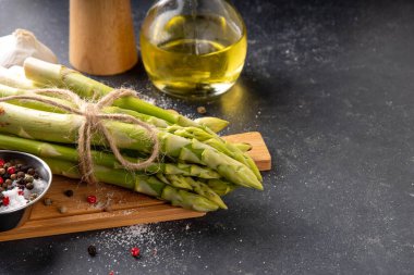 Çiğ organik kuşkonmaz mutfak masasının arka planında bir sürü ev yapımı yeşil kuşkonmaz pişirmeye ve kesme tahtasının üzerinde hazır. Yaz hasadı, yaz yemeği malzemeleri.