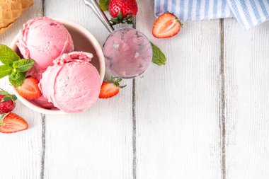 Yaz ferahlatıcı soğuk tatlı, lezzetli ve aromatik çilekli dondurma, seramik kasede ev yapımı meyve şerbeti, taze çilekler, beyaz ahşap arka planda dondurma külahları.
