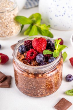 Çikolatalı Yulaf ezmesi, çikolata soslu, fındıklı ve taze dutlu, beyaz mutfak masasında yuvarlanmış yulaf, ahududu, yaban mersini, çilekli