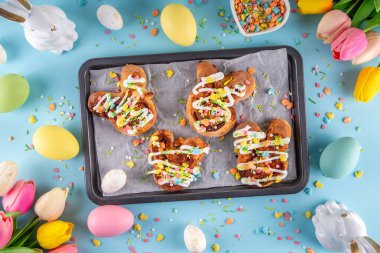 Tatlı ve lezzetli Paskalya tavşanı tarçınlı çörekler. Tatlı tavşan şekilli çörekler, renkli paskalya şekeri parçacıkları, paskalya süslemeleri, renkli yumurtalar ve tavşan tavşanları, kopya alanı