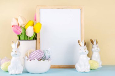 Bahar Paskalya bayramı masası boyalı Paskalya yumurtaları, bahar çiçekleri buketi, dekoratif tavşanlar, beyaz mutfak arka planında