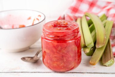 Pembe ve yeşil rengarenk tatlı reçel. Ev yapımı tatlı ravent konserveleri, beyaz ahşap masada küçük bir kavanozda, arka planda taze ravent ile.