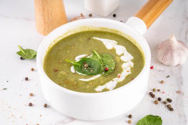 Lezzetli yeşil ıspanak kremalı çorba, kremalı ve taze ıspanak yapraklı. Lezzetli kremalı çorba, baharatlar ve beyaz masa arkasında zeytinyağı. Sağlıklı diyet bahar vejetaryen yemek tarifi