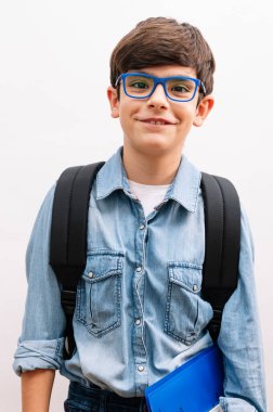 Sırt çantasıyla gezen güzel bir öğrenci çocuğu. Elinde kitaplarla izole edilmiş beyaz arka planda mutlu bir yüzle ayakta duruyor ve gülümsüyor.