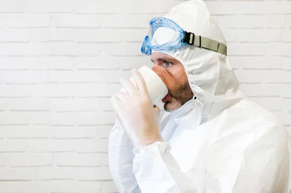 Male nurse wearing protective suit and work clothes drinking a cup of coffee during break