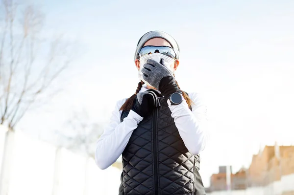 Sportsman putting on face mask in the industrial zone in winter while the sun rises.