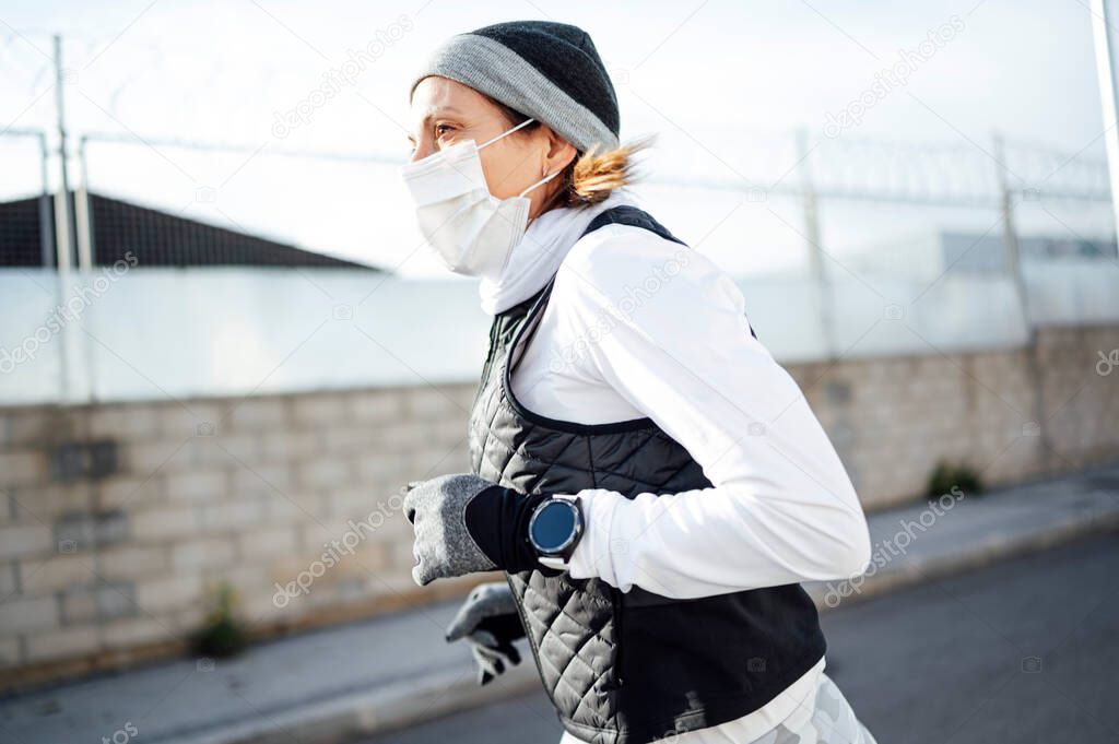 Sportsman with mask running through the industrial zone in winter as the sun rises.