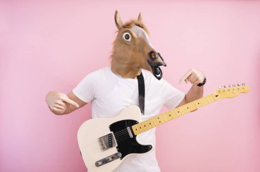 At maskeli bir adam elektro gitarı işaret ediyor.