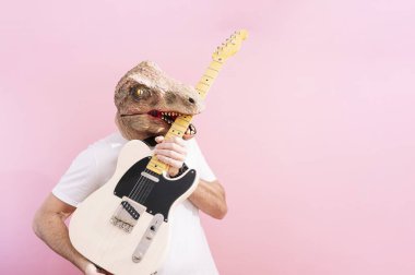 Kertenkele maskeli adam elektro gitarı ısırıyor.