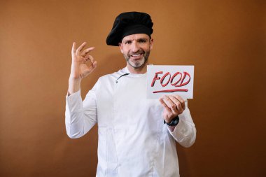 Şef elinde yemek yazan bir tabela tutuyor.