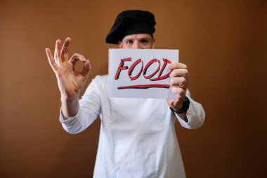 Şef elinde yemek yazan bir tabela tutuyor.