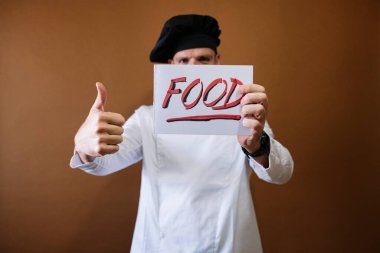 Şef elinde yemek yazan bir tabela tutuyor.