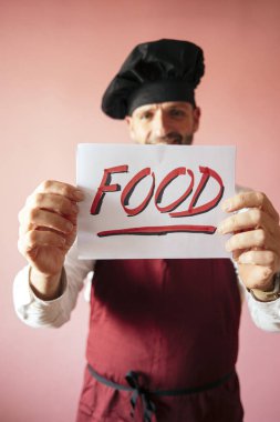 Şef elinde yemek yazan bir tabela tutuyor.