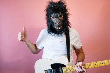 Goril maskeli ve elektro gitarlı bir adam baş parmağını gösteriyor.