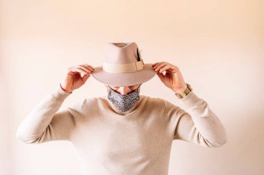 Koronavirüs sırasında bej arka planda çiçek maskeli ve şapkalı bir adam.