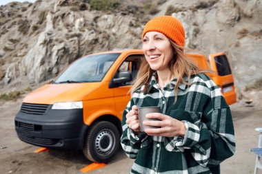 Turuncu minibüsüyle plajda gezen bir kadın.