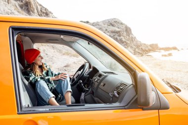 Turuncu minibüsüyle plajda gezen bir kadın.