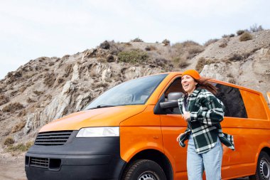 Turuncu minibüsüyle sahilde tatilde olan mutlu kadın.