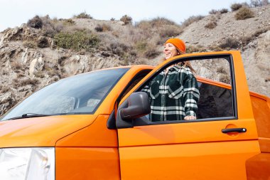 Turuncu minibüsüyle sahilde tatilde olan mutlu kadın.