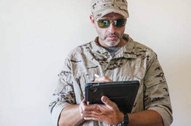 Kamuflaj üniformalı beyaz adam tablet kullanıyor. Teknoloji konsepti..