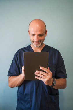 Tablet sağlık görevlisiyle gülümseyen doktorun stüdyo portresi.