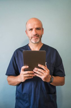 Tablet sağlık görevlisiyle gülümseyen doktorun stüdyo portresi.