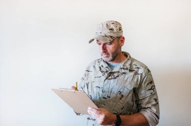 Kamuflaj üniformalı beyaz adam deftere yazıyor..