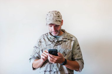 Caucasian man in camouflaged army uniform using a smart phone, technology concept.
