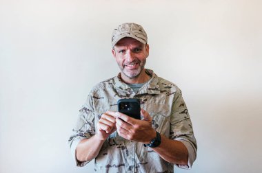 Caucasian man in camouflaged army uniform using a smart phone, technology concept.