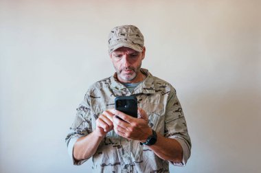 Caucasian man in camouflaged army uniform using a smart phone, technology concept.