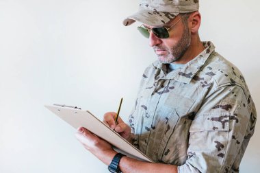 Kamuflaj üniformalı beyaz adam deftere yazıyor..