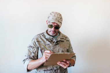 Kamuflaj üniformalı beyaz adam deftere yazıyor..