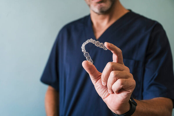 Мужчина-врач держит прозрачный стоматологический выравниватель рукой