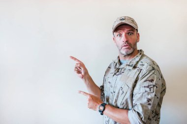 Kamuflajlı üniformalı, iki eli ve parmakları yanda olan şaşırmış bir adam..