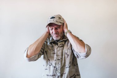 Bomba seslerini duymamak için kulaklarını kapatan kamuflajlı asker üniforması giyen beyaz bir adam..