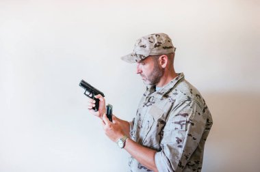 Askeri üniformalı yakışıklı adam kamufle oldu ve silaha cephane koydu..