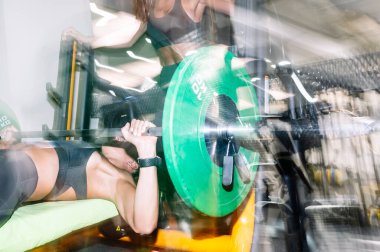 Spor salonunda iki kadın antrenman yapıyor, göğsüyle ağırlık kaldırıyor..