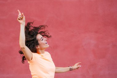 Kollarıyla duvarın önünde dans eden neşeli bir kadın.