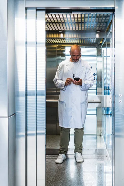 Scientist dressed in a white coat using the smart phone inside an elevator.