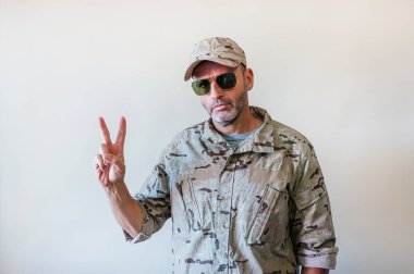 Kamuflaj üniformalı beyaz adam parmaklarını V şeklinde gösteriyor, zafer konsepti..
