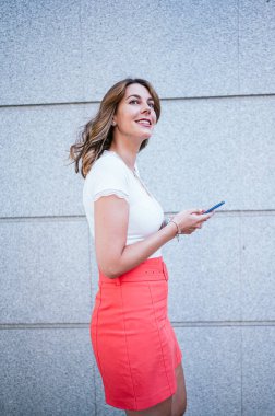 Yazlık giysiler giymiş, akıllı telefon kullanan ve şehirde dikilen kadınların yan görüntüsü..