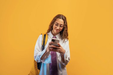 Öğrenci telefonu kontrol ediyor, okul üniforması giyiyor..