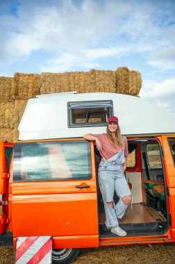 Turuncu karavanın yanında dinlenen şapkalı bir kadın..