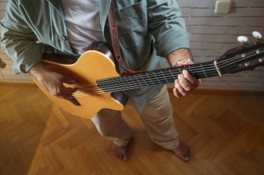 Çıplak ayaklı adam tahta zeminde akustik gitar çalıyor..