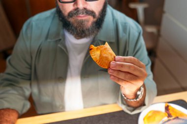 Masada otururken ısırılmış börek tutan adam..