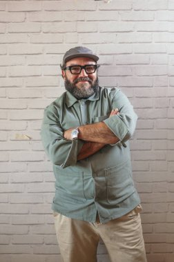 Tuğla duvara yaslanmış kollarıyla gülümseyen bir adam..